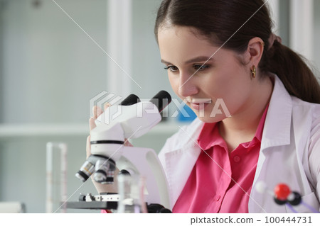 Close up of young scientist looks through microscope in laboratory. 100444731