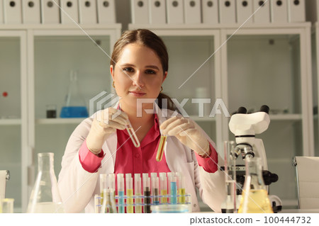 Young chemist holds two test tubes with different liquids and looks at camera. 100444732