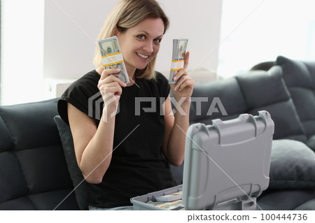 Smiling woman with suitcase full of money holding stacks of dollar bills and looking at camera. Smiling woman with suitcase full of money holding stacks of dollar bills and looking at camera. 100444736