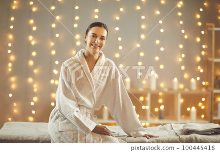 Young pretty woman in bathrobe sitting on massage table in spa salon. Wellness concept. 100445418