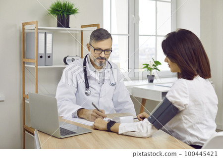 Man doctor gives prescription after checking blood pressure of young woman patient Man doctor gives prescription after checking blood pressure of young woman patient 100445421
