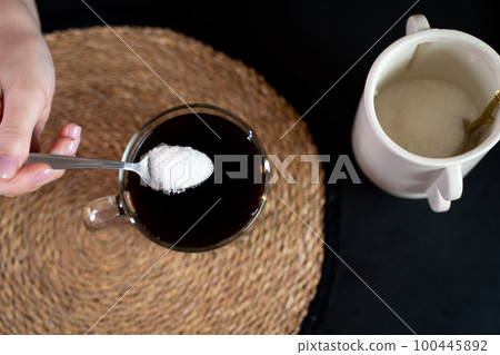 Top view of a woman's hand holding a spoon in her hand, pouring sugar into a coffee cup Top view of a woman's hand holding a spoon in her hand, pouring sugar into a coffee cup 100445892