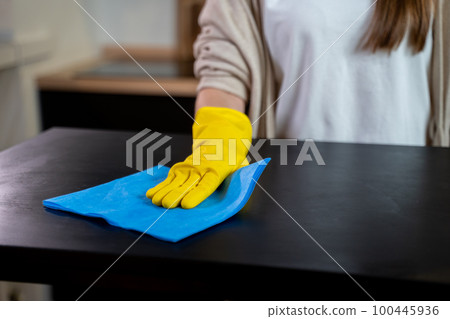 Cleaning service worker cleans the kitchen table at home. Beautiful young female housekeeper wipes dirty table Cleaning service worker cleans the kitchen table at home. Beautiful young female housekeeper wipes dirty table 100445936