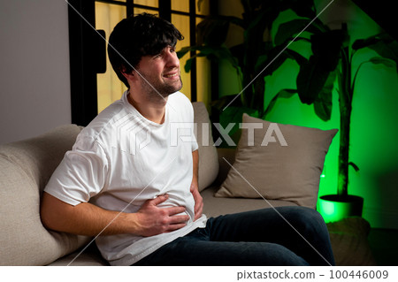 Man suffering stomachache sitting on a couch in the living room at home 100446009