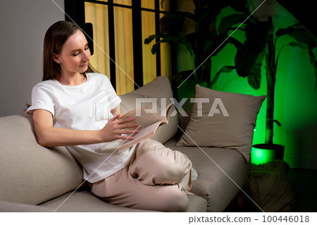 Thoughtful, relaxed woman is reading a book sitting on the couch. Thoughtful, relaxed woman is reading a book sitting on the couch. 100446018