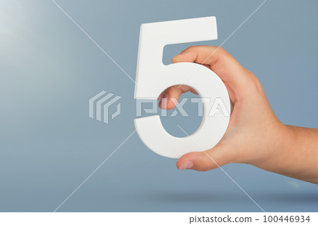 Number five in hand. Hand holding white number 5 on blue background with copy space. Concept with number five. Birthday 5 years, fifth grade, five day work week Number five in hand. Hand holding white number 5 on blue background with copy space. Concept with number five. Birthday 5 years, fifth grade, five day work week 100446934