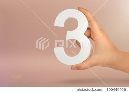 Number three in hand. Hand holding white number 3 on red background with copy space. Concept with number three. 3 percent, birthday 3 years, third grade, triple 100446936