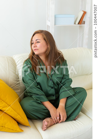 Cute female model in pajama enjoying morning. Pleasant woman sitting on sofa. Good mood Cute female model in pajama enjoying morning. Pleasant woman sitting on sofa. Good mood 100447007