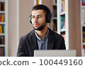 Man with eyeglasses and headphones working on laptop in library 100449160