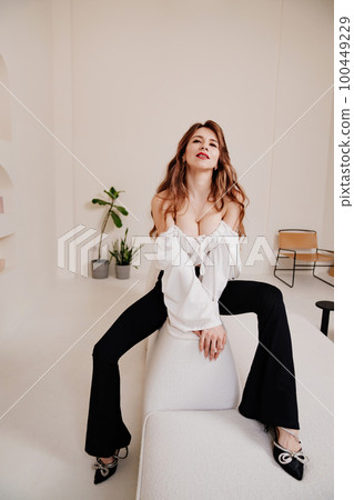 an attractive woman in a white top and black pants sits on a white sofa. an attractive woman in a white top and black pants sits on a white sofa. 100449229