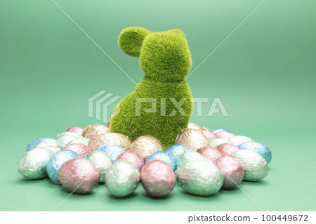 Green bunny, rabbit surrounded by small Easter chocolate eggs, sweets wrapped in colorful bright foil green blue background. Religious Happy Easter concept. Closeup, horizontal plane Green bunny, rabbit surrounded by small Easter chocolate eggs, sweets wrapped in colorful bright foil green blue background. Religious Happy Easter concept. Closeup, horizontal plane 100449672