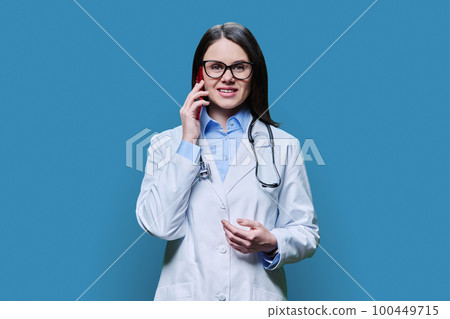 Young female doctor talking on mobile phone, on blue background Young female doctor talking on mobile phone, on blue background 100449715