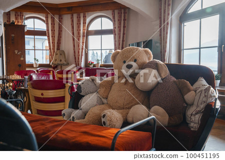Teddy bear with stuffed toys arranged on sofa by armchairs with windows in the background inside luxurious hotel room 100451195