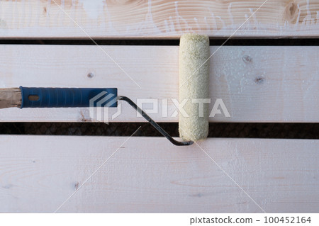 White paint roller applicator brush with handle painting wooden fence, floor plank. Cosmetic repair, house renovation White paint roller applicator brush with handle painting wooden fence, floor plank. Cosmetic repair, house renovation 100452164