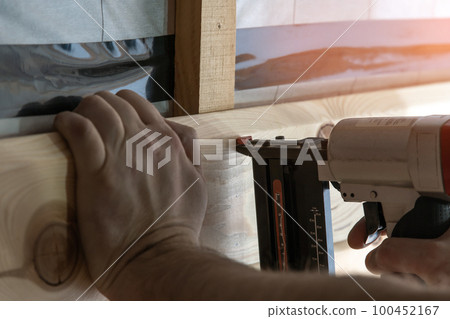 Cropped builder hands holding pneumatic nail gun, stapler for wooden board. Scoring, set up metal staples. Handiman work 100452167