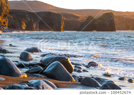 Scenic Beach with Black Sand by Low Tide at Sunset. Volcanic Mountains and Cliffs in Golden Sun Rays. Atlantic Ocean Coastline. Kopasker, Iceland.  100452674