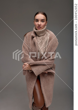 Fashion young woman in a faux fur coat on a gray background. 100452852