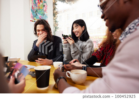 A company of young people in a cafe, have fun, drink coffee, have fun browsing social networks with a cheerful company, modern young people with laptops and smartphones A company of young people in a cafe, have fun, drink coffee, have fun browsing social networks with a cheerful company, modern young people with laptops and smartphones 100452925