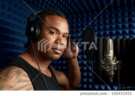 Close-up of an afro american rap artist with headphones while recording a song at a recording studio Close-up of an afro american rap artist with headphones while recording a song at a recording studio 100452955