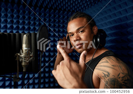 Close-up of an afro american rap artist with headphones while recording a song at a recording studio Close-up of an afro american rap artist with headphones while recording a song at a recording studio 100452956