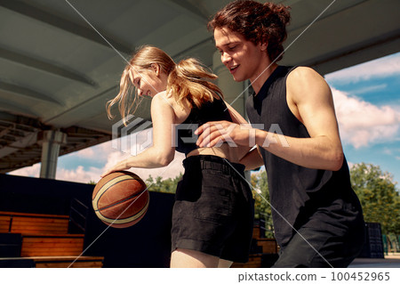 Young people play basketball on the street, a girl and a guy play streetball on the city playground Young people play basketball on the street, a girl and a guy play streetball on the city playground 100452965