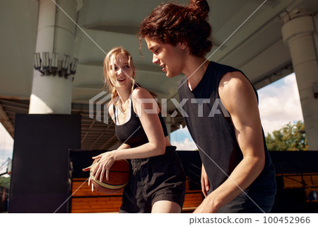 Athletic young people play streetball on the street, a girl and a guy play basketball on the city playground. 100452966