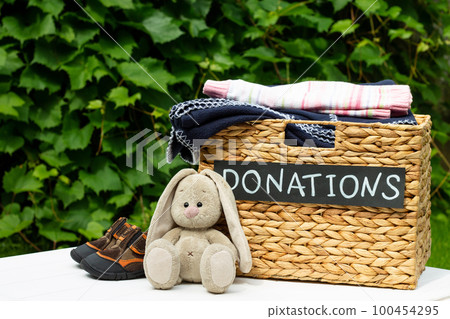 Donation box with children shoes and toy hare on a greenery background. Charity and donation concept. Copy space. Donation box with children shoes and toy hare on a greenery background. Charity and donation concept. Copy space. 100454295