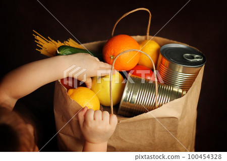 Little girl puts products in a paper bag on a brown background. Little girl puts products in a paper bag on a brown background. 100454328
