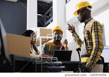 African american logistics managers team dicussing goods distribution at warehouse reception. Post office men and woman workers planning stock supply while chatting at counter desk 100454998