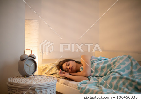 The woman sleeps in her bed with the bedside lamp lit. The woman sleeps in her bed with the bedside lamp lit. 100456333