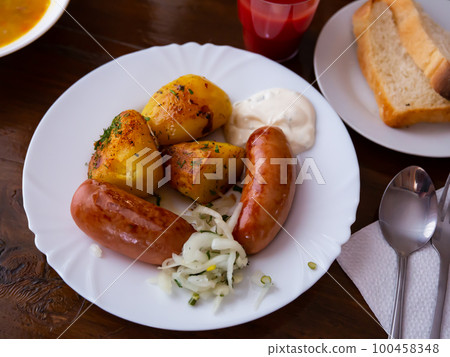 Grilled meat sausages served with potatoes fried with onion Grilled meat sausages served with potatoes fried with onion 100458348
