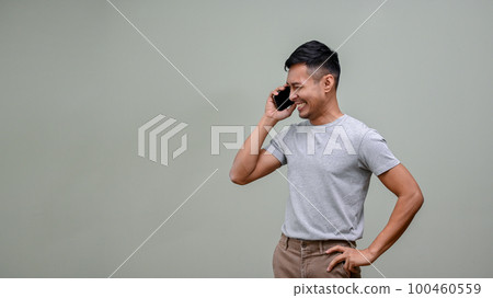 Smiling Asian man looking aside and talking on the phone with someone, isolated background Smiling Asian man looking aside and talking on the phone with someone, isolated background 100460559