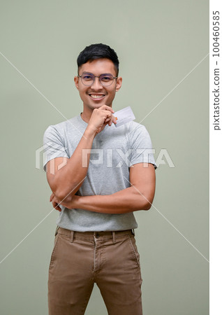 Smiling Asian man holding a credit card while standing against an isolated green background Smiling Asian man holding a credit card while standing against an isolated green background 100460585
