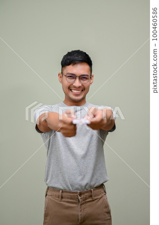 Smiling Asian man handing a credit card to the camera while standing against an isolated background. Smiling Asian man handing a credit card to the camera while standing against an isolated background. 100460586