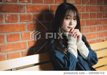 A girl sitting on a bench in front of a red brick A girl sitting on a bench in front of a red brick 100466710