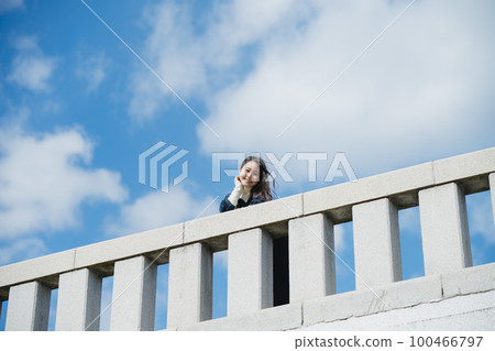 A woman standing on a bridge against the blue sky A woman standing on a bridge against the blue sky 100466797