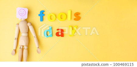 Yellow background with a wooden doll with a smile fools day, April 1. Copy space 100469115