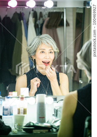 Gray-haired woman applying makeup 100469927