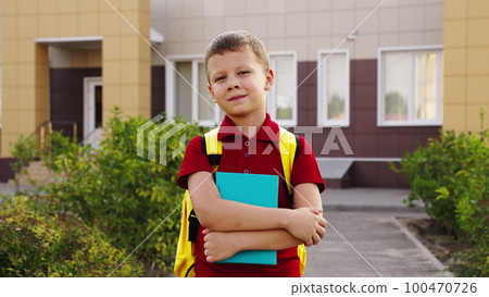 teenage boy with textbook his hands smiles. portrait happy schoolboy with book. educational school program for children. cheerful kid boy school yard. student with school backpack his back. close-up. teenage boy with textbook his hands smiles. portrait happy schoolboy with book. educational school program for children. cheerful kid boy school yard. student with school backpack his back. close-up. 100470726