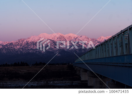 被夕陽和北阿爾卑斯茂胜山的雪景染紅的常願寺川大日橋 100471435