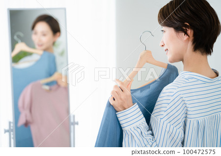 Fashion image of a young woman choosing clothes in front of a mirror Fashion image of a young woman choosing clothes in front of a mirror 100472575