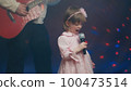Little girl on stage in vintage dress, she sings into microphone and dances, her father plays acoustic guitar. Color music is shining and smoke is billowing. Father and Child Day, performance on stage 100473514