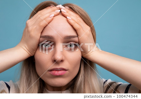close-up of an upset girl in casual clothes holding her head on a blue isolated background close-up of an upset girl in casual clothes holding her head on a blue isolated background 100474344