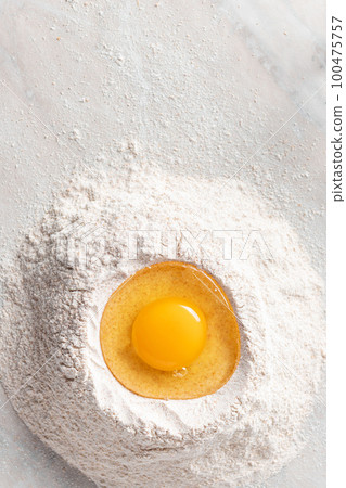Fresh egg in heap of wholemeal flour on marble table Fresh egg in heap of wholemeal flour on marble table 100475757