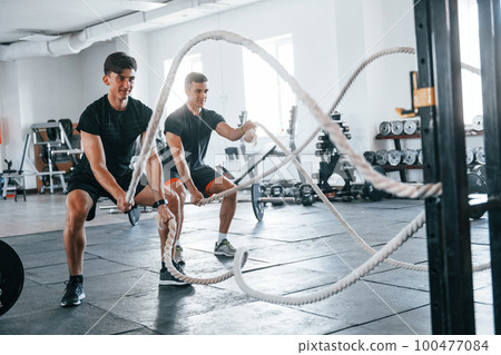 Young people with sportive body shapes doing crossfit by using knots Young people with sportive body shapes doing crossfit by using knots 100477084