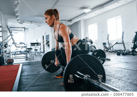 Young fitness woman with slim type of body doing exercises by using barbell 100477805