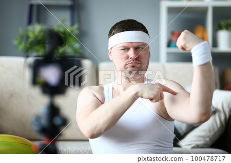 Energetic joyful male blogger measuring bicep size while smiling and updating blog Energetic joyful male blogger measuring bicep size while smiling and updating blog 100478717