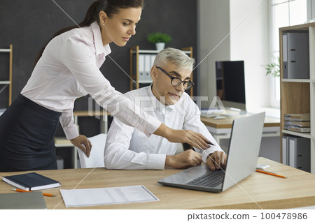 Young woman director views the project of the employee on the laptop screen, shows the inaccuracies of the project. 100478986