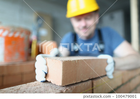 Bricklayer builder worker laying brick wall of house 100479001