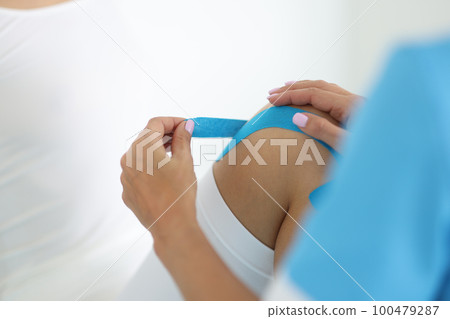 Physiotherapist applying kinesiotape to patient knee closeup Physiotherapist applying kinesiotape to patient knee closeup 100479287